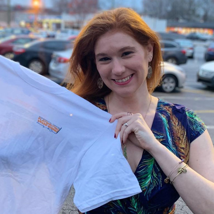 Emily McClain holds up her 2019 Playwriting Award Winner t-shirt